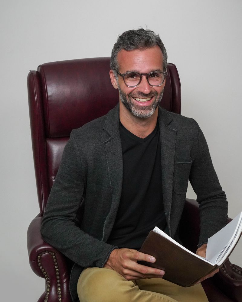 Mike Moll smiling in a leather armchair with a notebook