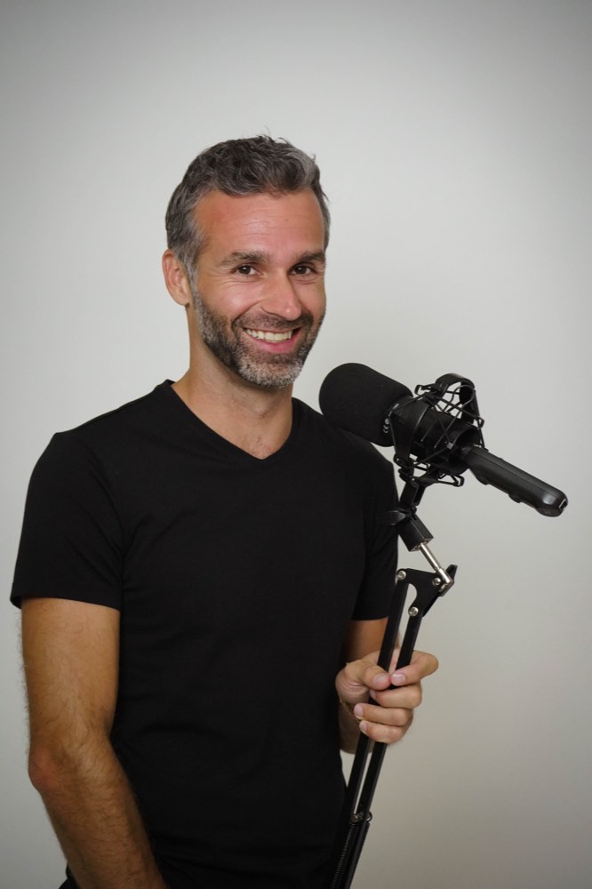 Mike Moll smiling beside a podcast microphone